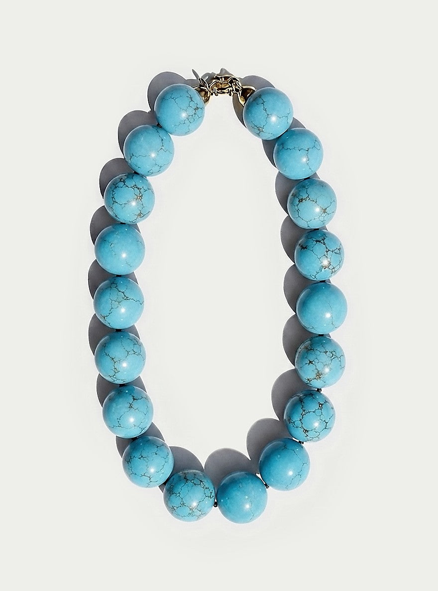 A beaded necklace made of large, round turquoise-blue marbled beads with a small gold-toned clasp, displayed on a light gray background with soft drop shadows.