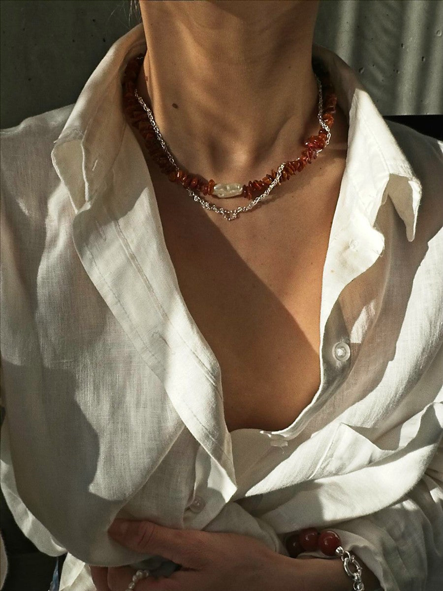 Close-up of a person wearing a white shirt with an amber necklace and bracelet.