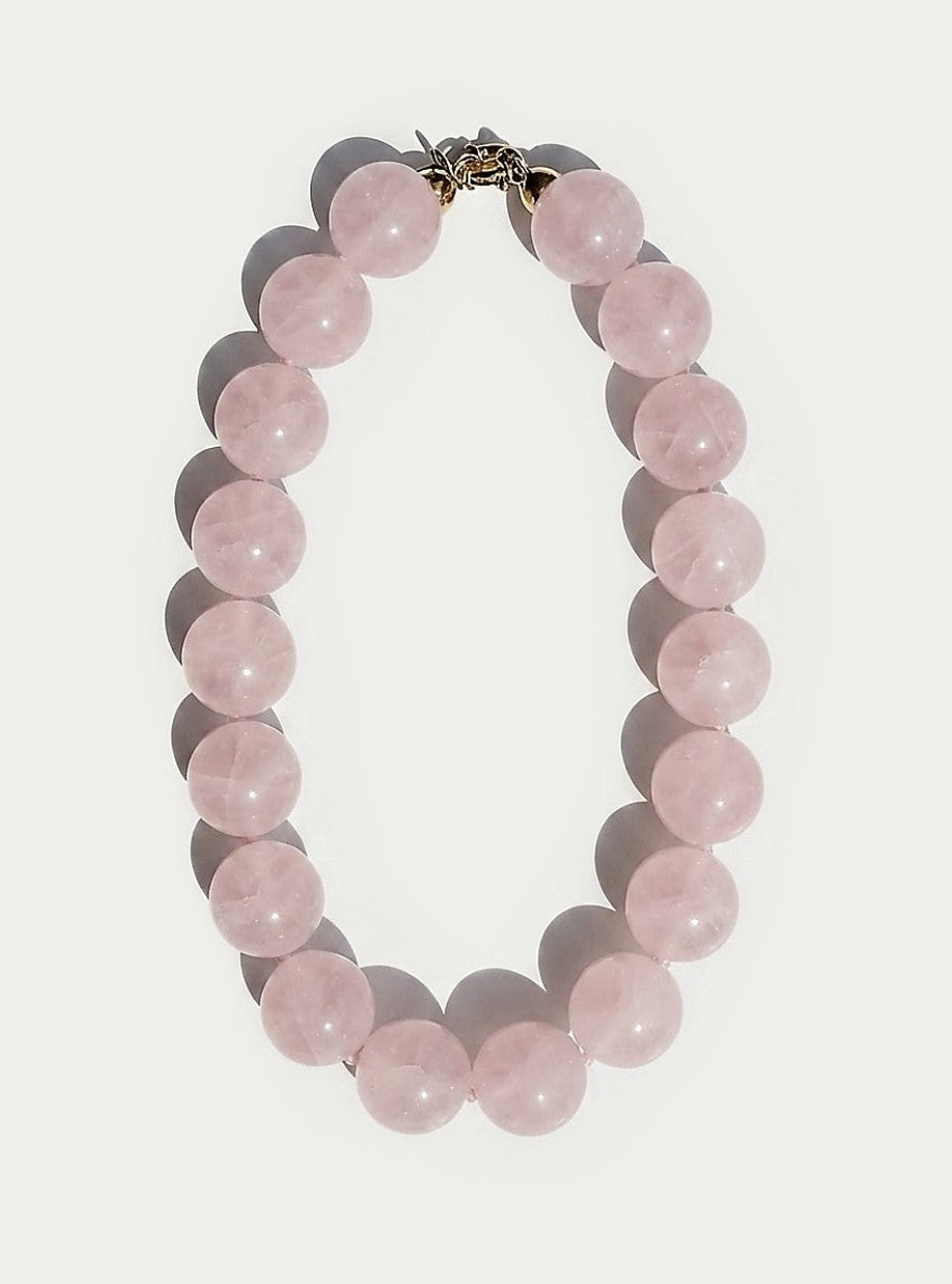 A beaded necklace made of smooth, round pale pink stones with a small metallic clasp, shown on a plain light background.